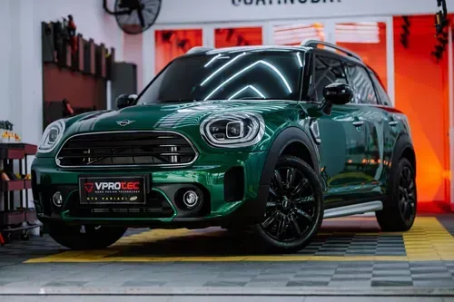 A dark green Mini Countryman parked in a bright garage with a tiled floor and orange wall panels.