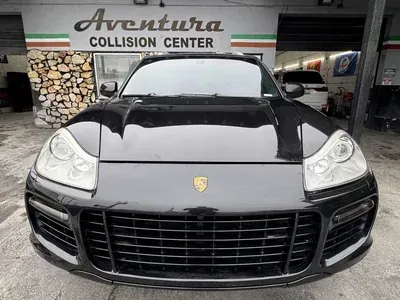 A black Porsche Cayenne parked in front of the Aventura Collision Center building.