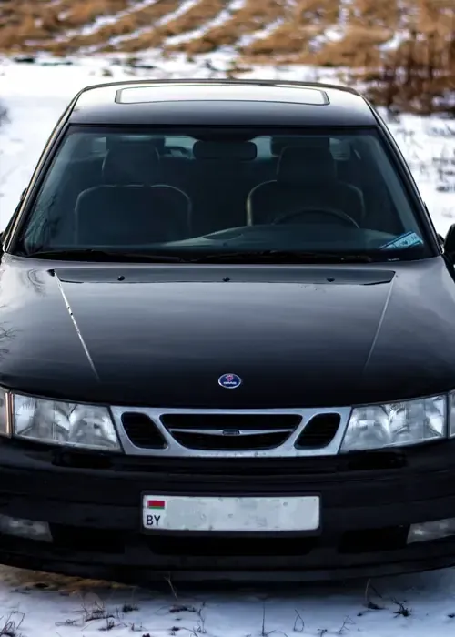 A black Saab 9-3 car is parked on a snowy, open field.