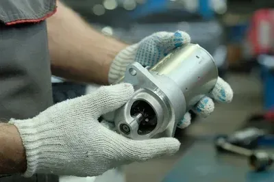 A mechanic's hands work on an alternator installed inside a vehicle's engine bay.