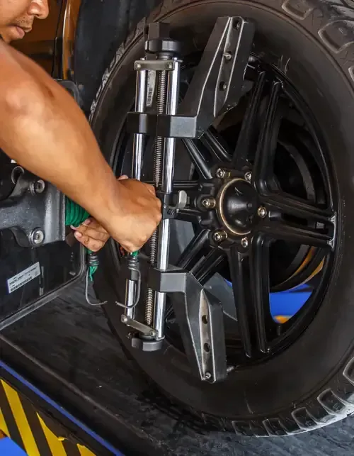 A technician attaches a wheel alignment sensor to a black vehicle wheel in a service shop.