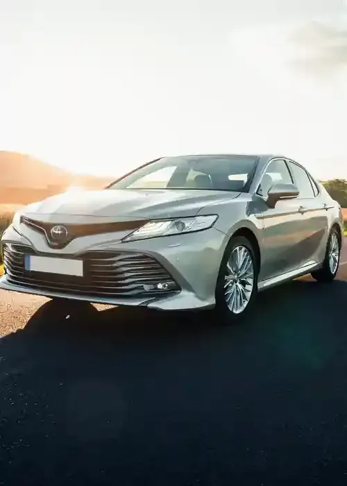 A silver Toyota Camry sedan parked on an asphalt road during a sunset.