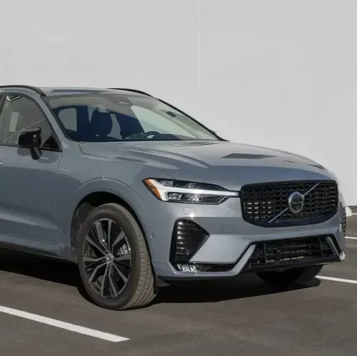 A grey Volvo XC60 SUV parked in a paved lot against a plain white wall.