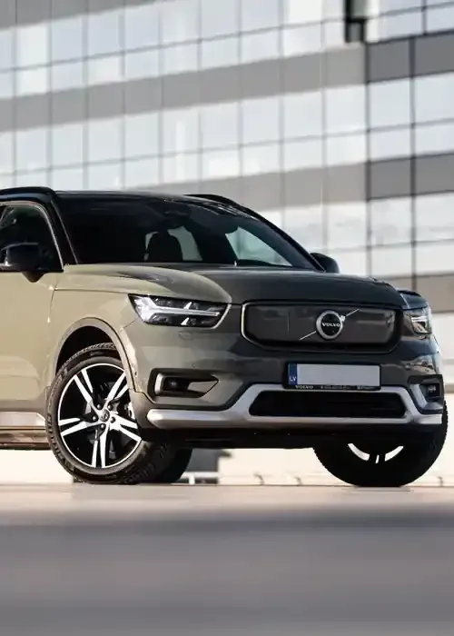A sage green Volvo XC40 Recharge SUV parked on a rooftop level with a glass office building in the background.