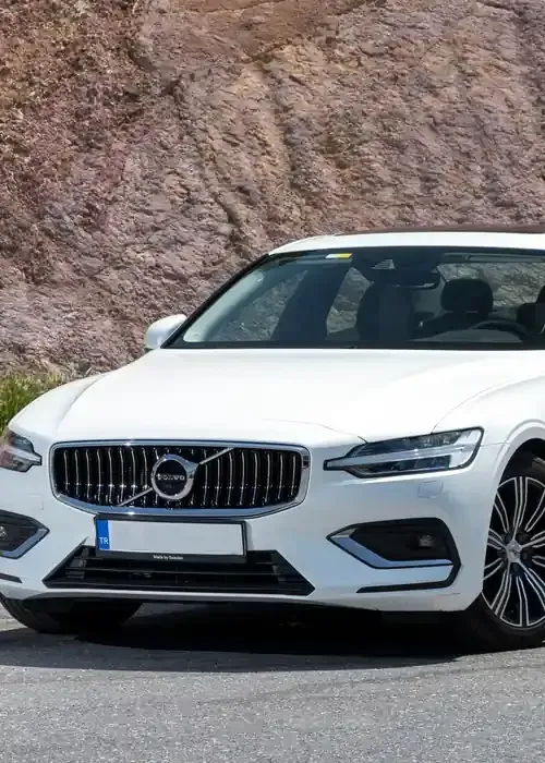 A white Volvo sedan parked against a rocky hillside background.