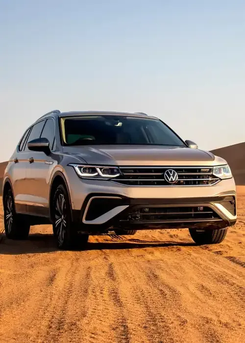 A silver Volkswagen Tiguan SUV parked on a sandy desert landscape under a clear sky.