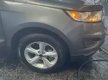 Gray SUV front wheel and headlight, parked on wet pavement.