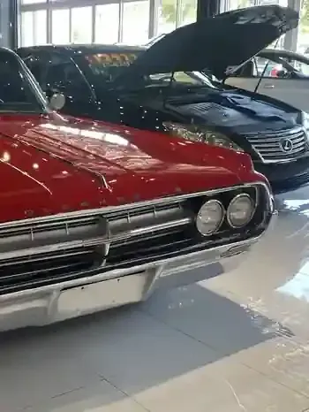 Red classic car in a showroom, with its hood open beside a black Lexus.