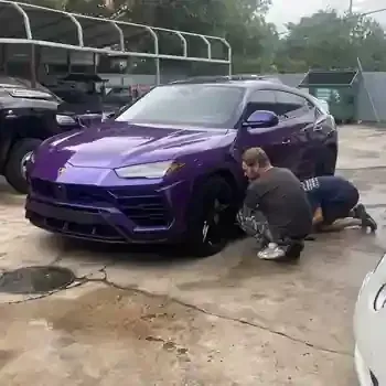 Two people washing a purple sports SUV in a wet parking lot