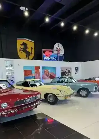 Classic cars displayed in a showroom with Ferrari and Pontiac signs on the wall.