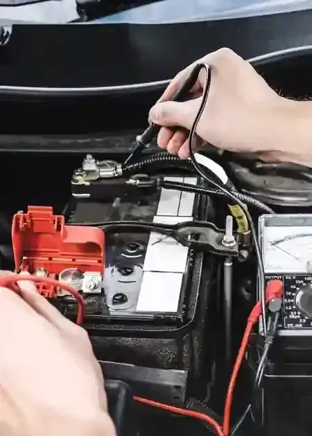 Hands connecting cables to a car battery, with red and black clamps in the engine bay