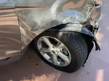 Severely damaged silver car wheel and crushed front fender after a collision