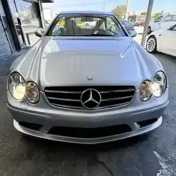 Front view of a silver Mercedes-Benz parked outside a dealership, headlights on