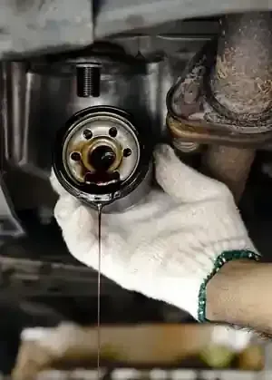 Gloved hand removing an oil filter with oil dripping from an engine underside