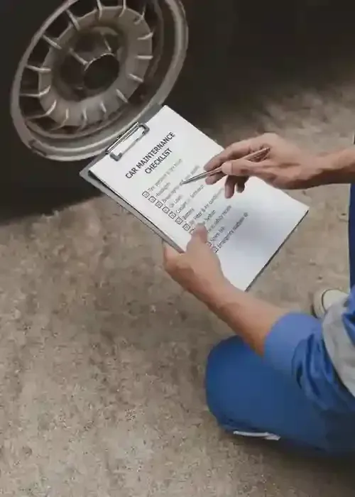 Person in blue uniform checks a clipboard beside a car wheel and tire.