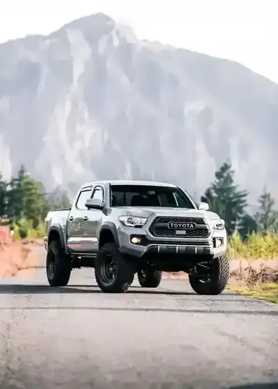 White lifted pickup truck parked on a road with mountains in the background