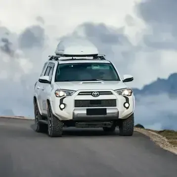 White SUV with roof cargo driving on a winding mountain road under cloudy skies