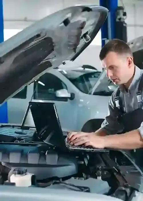Mechanic using a laptop to diagnose a car with its hood open in a repair shop