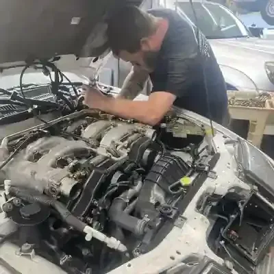 Mechanic working under a car’s open hood in a repair shop with engine parts exposed