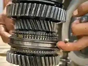 Close-up of stacked metal gears and shafts being assembled by hands in a workshop