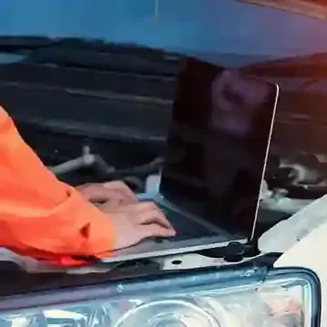 Person working on a laptop over a car engine under the hood
