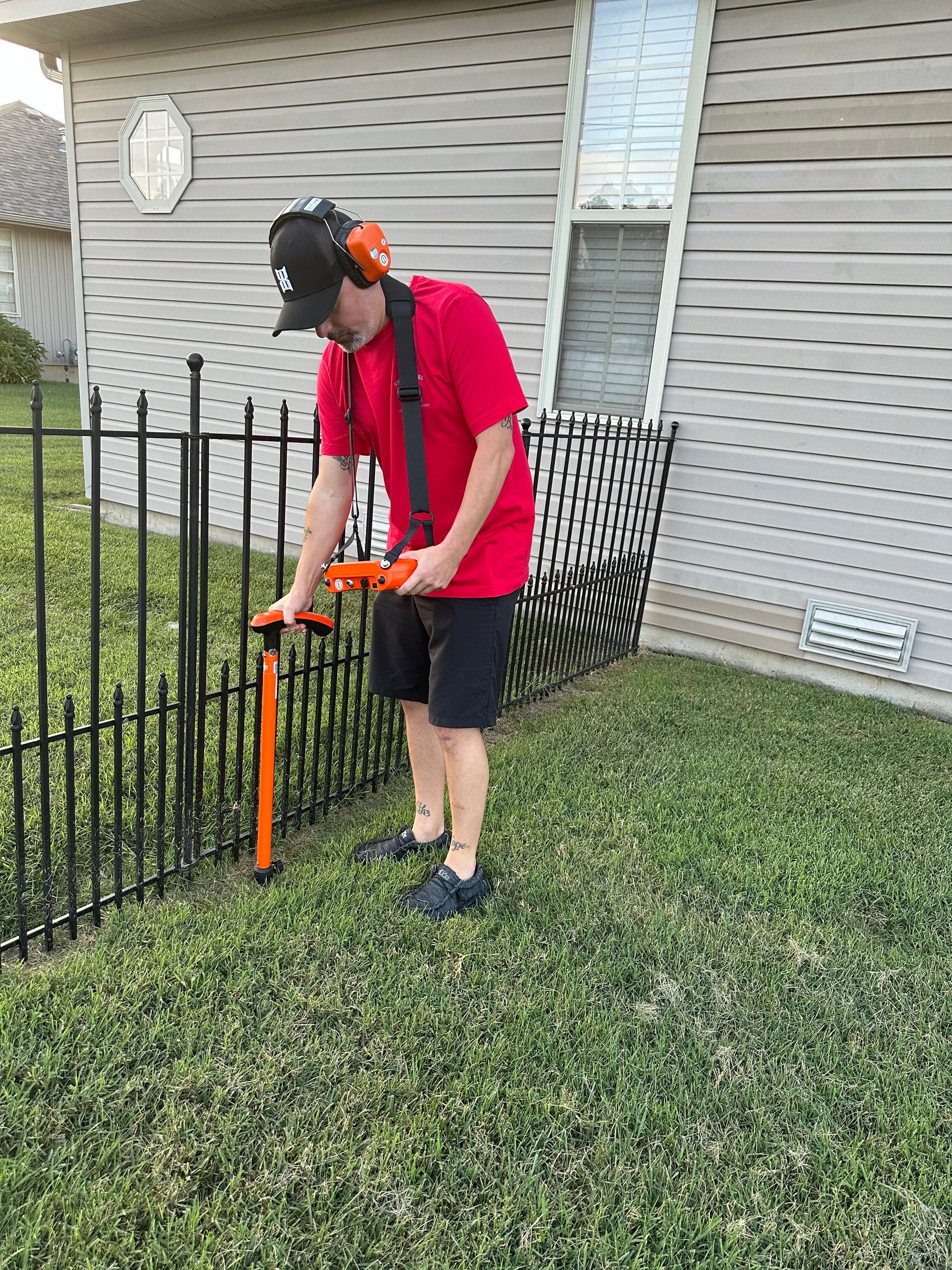 A man in a red shirt is standing on a sidewalk holding a tool.
