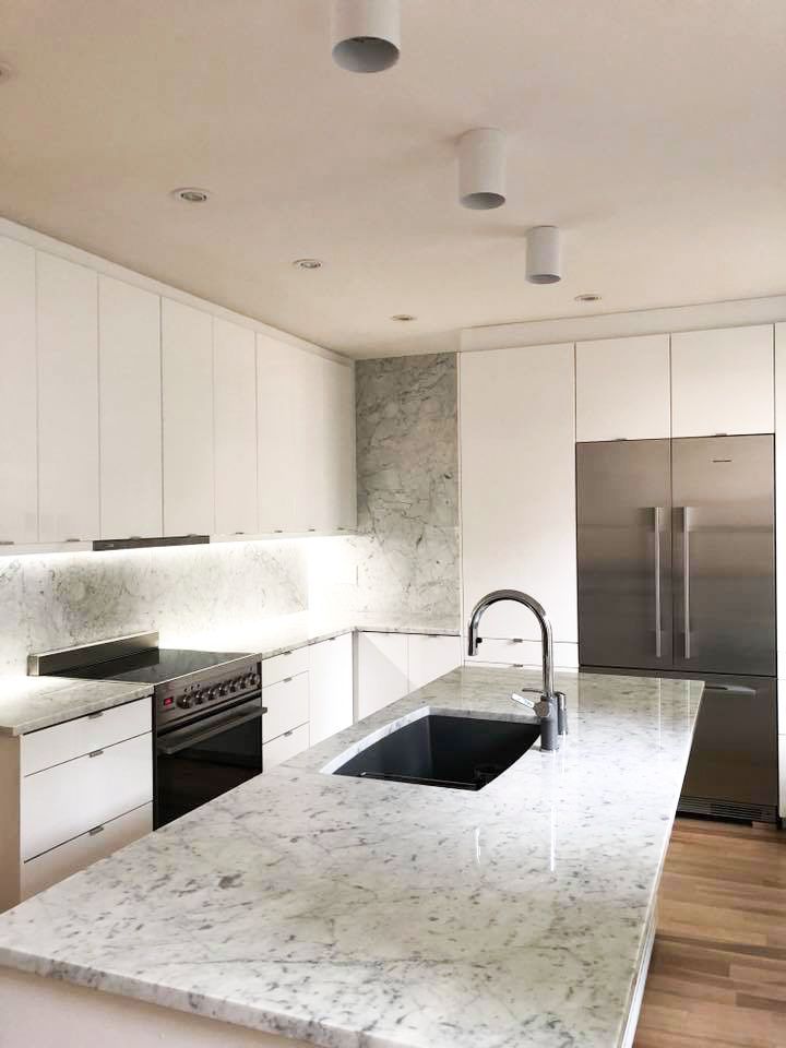 Une cuisine avec des armoires blanches, des comptoirs en granit, des appareils électroménagers en acier inoxydable et un grand îlot.