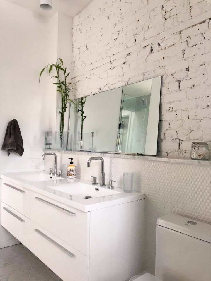 Une salle de bain avec deux lavabos et un WC avec un mur en briques blanches