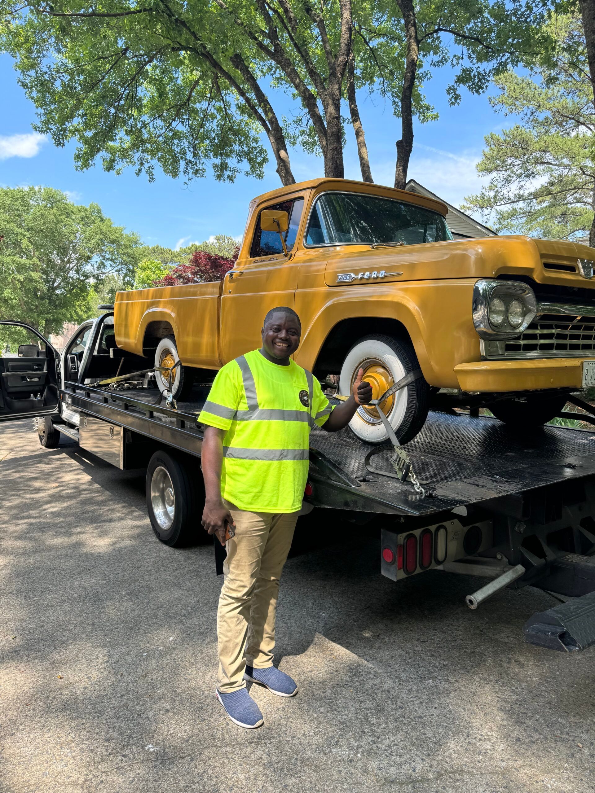 A man is standing in front of a yellow truck on a tow truck.