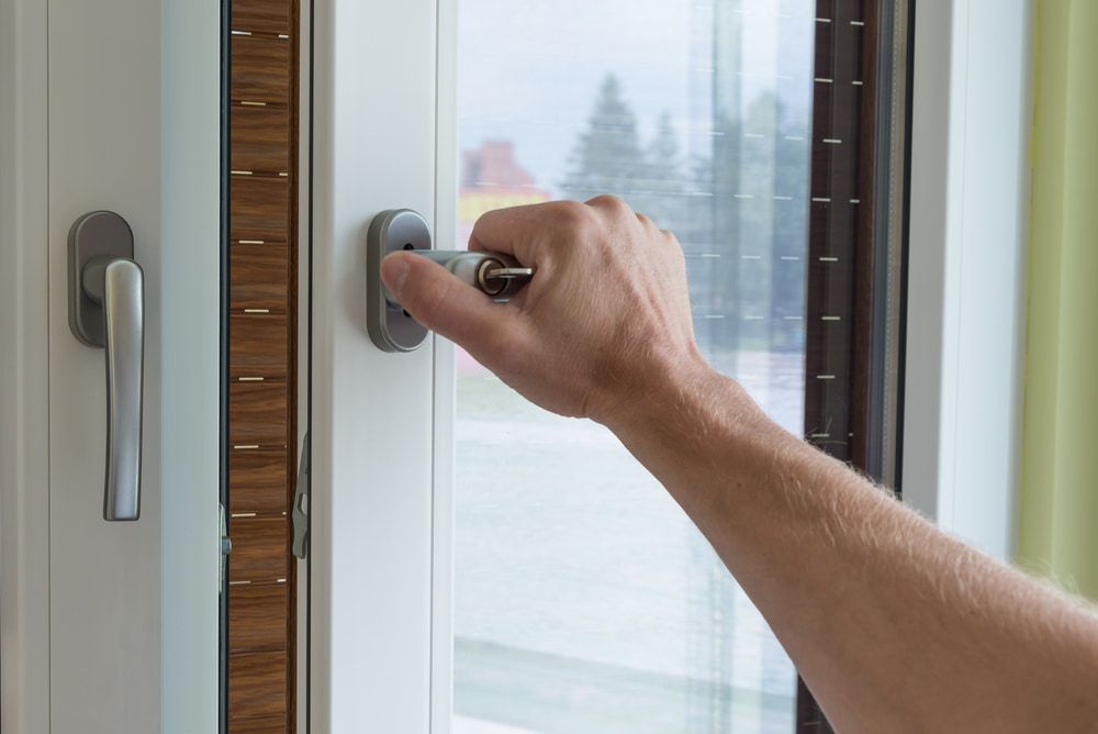 A Hand Turns a Silver Key in the Lock of a White-framed Window — ACG Windows & Glass in Mount Eliza, VIC