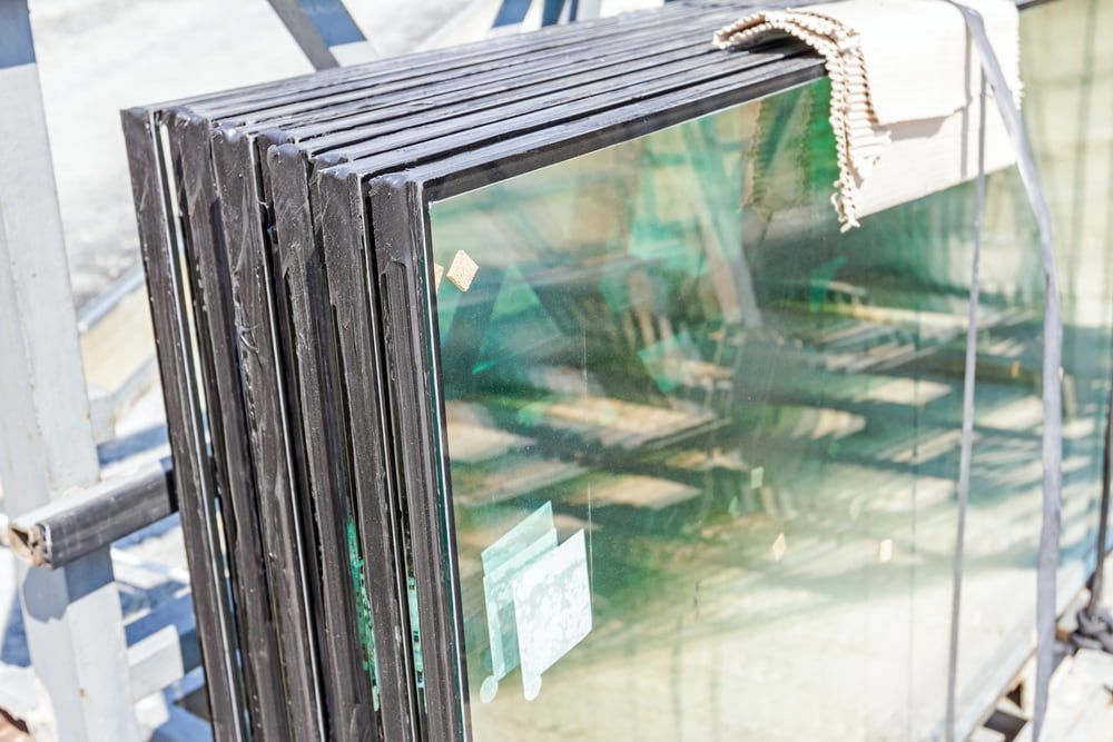 Stacked glass panes with dark edges, leaning on a metal rack outdoors. — ACG Windows & Glass in Lyndhurst, VIC