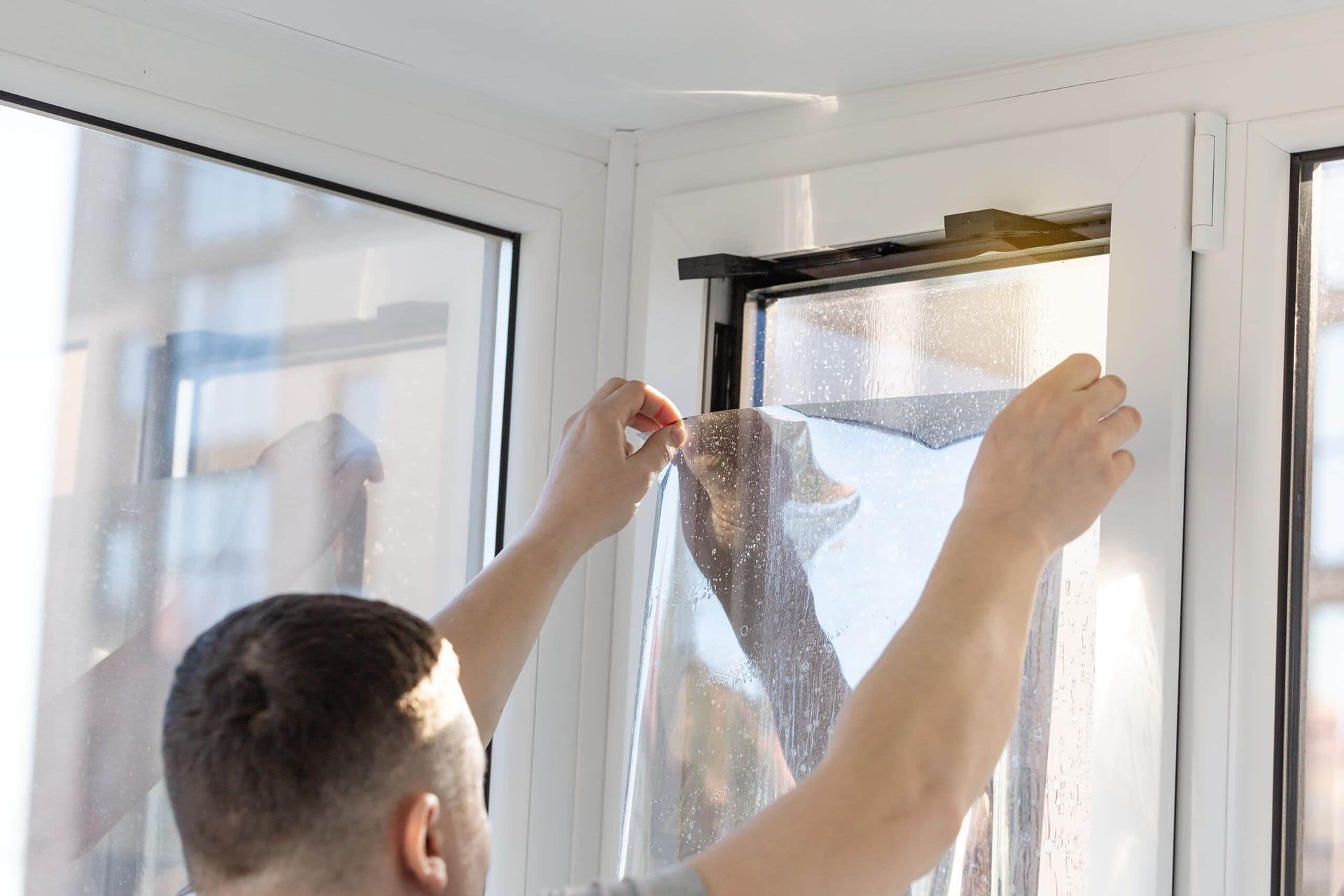 A Person Applying a Reflective Tint Film to a White-framed Window Pane — ACG Windows & Glass in Chelsea, VIC