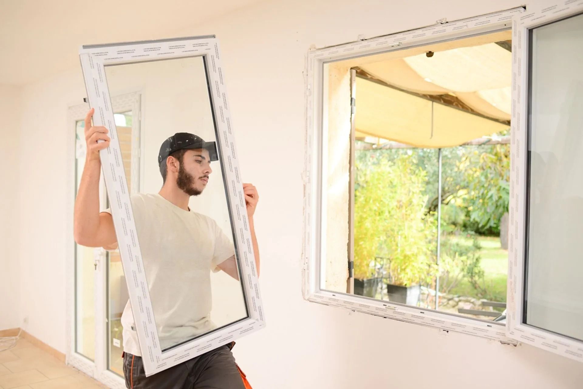 Man holding a window frame while installing a large window in a bright room — ACG Windows & Glass in Lyndhurst, VIC