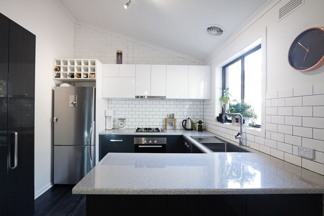 Modern kitchen with white cabinets, black island, stainless fridge, and window above the sink — ACG Windows & Glass in Cranbourne, VIC