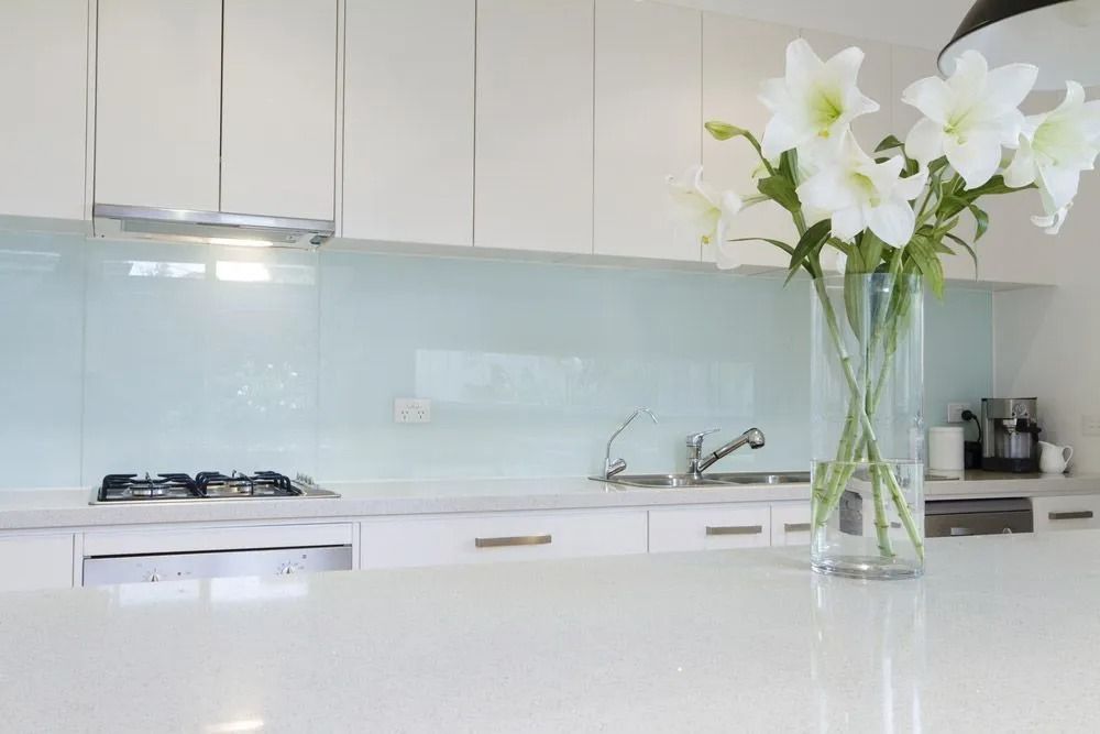 Bright modern kitchen with white cabinets, glass backsplash, and a vase of white flowers on the counter — ACG Windows & Glass in Cranbourne, VIC