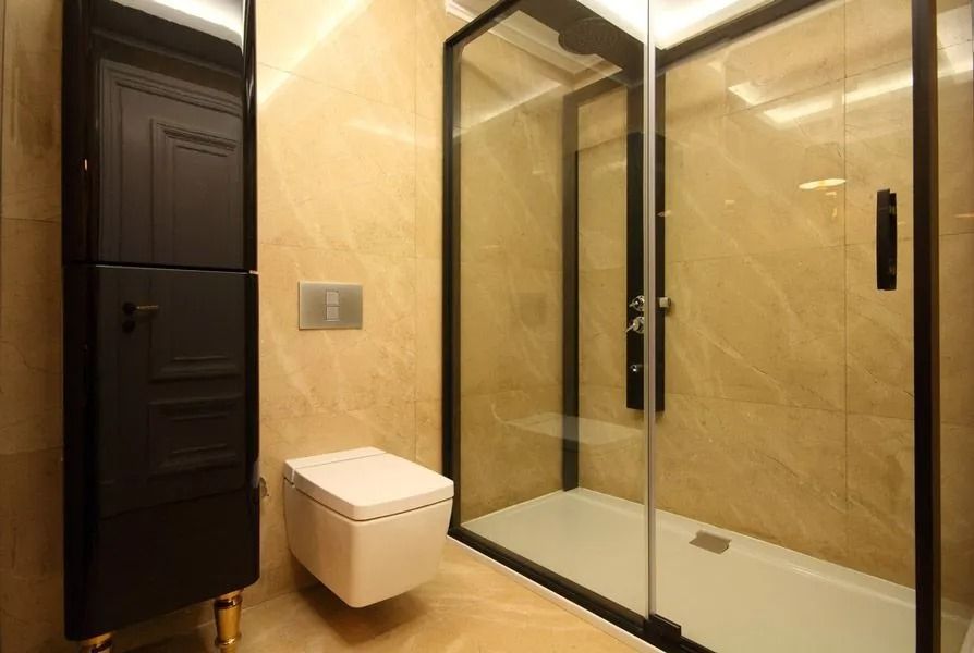 Modern bathroom with glass shower enclosure, beige marble walls, and a wall-mounted toilet beside a dark door — ACG Windows & Glass in Lyndhurst, VIC