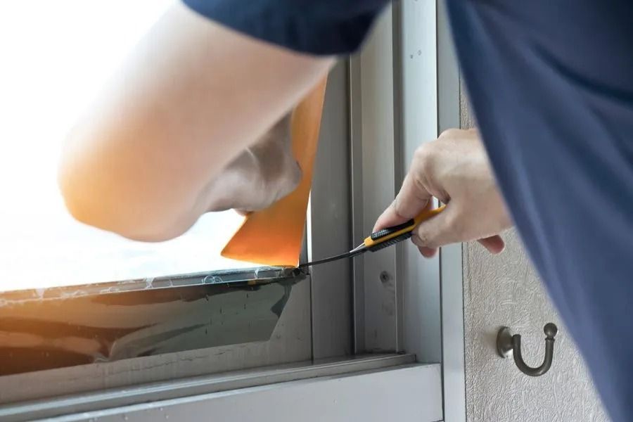 A Person Uses a Utility Knife to Trim a Piece of Orange Material — ACG Windows & Glass in Lyndhurst, VIC