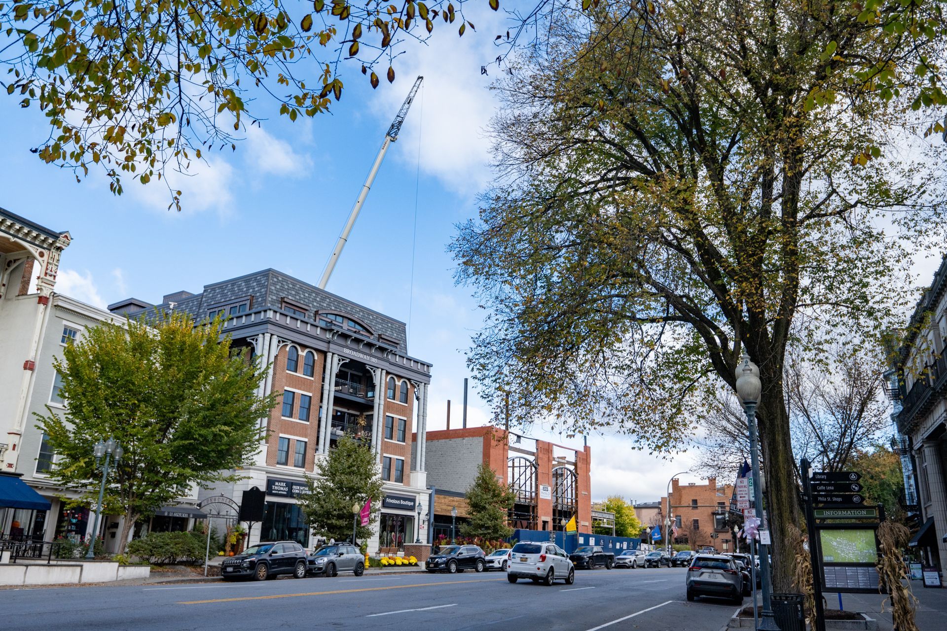A city street with a crane in the background and cars driving down it.