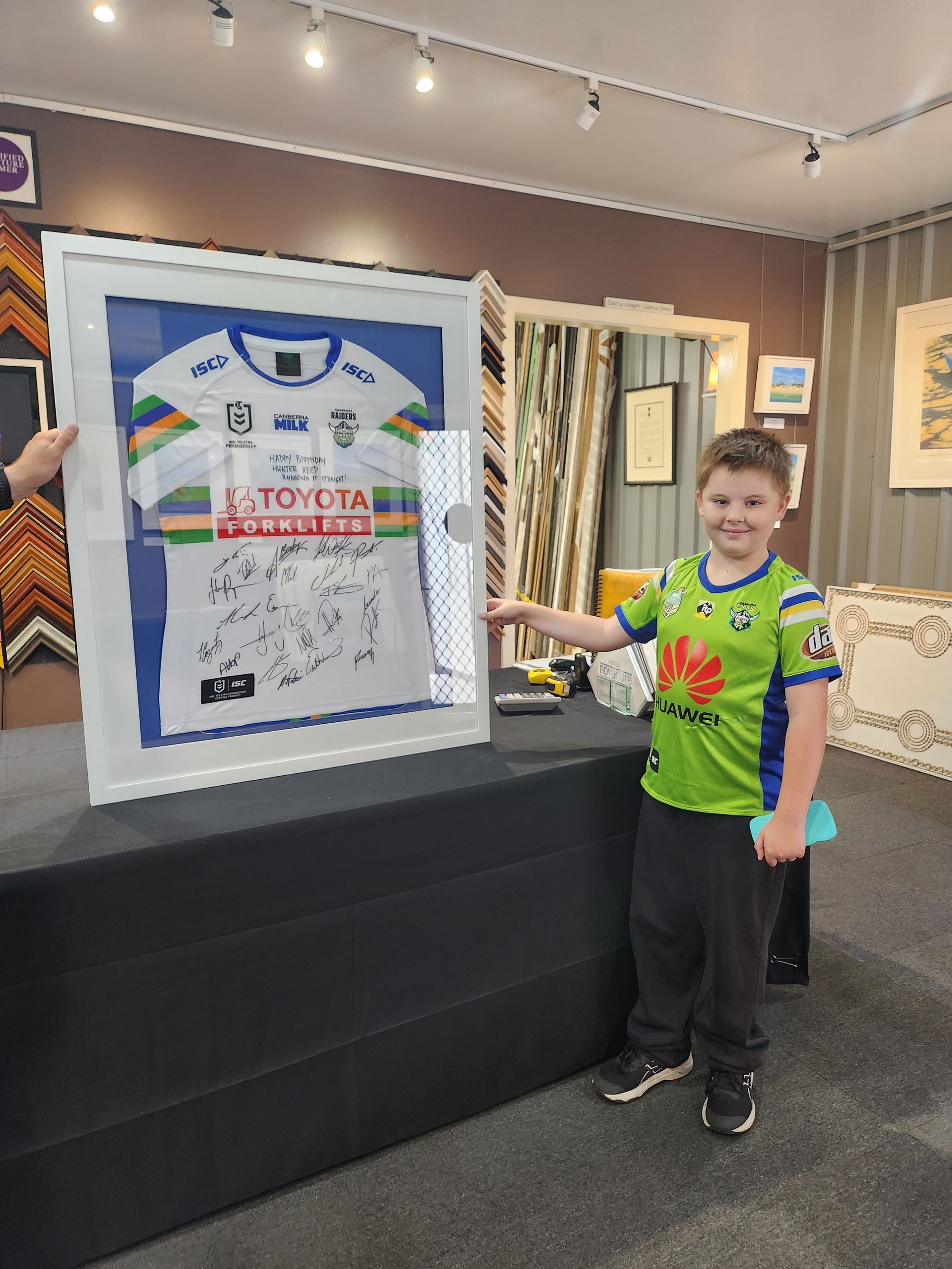 A young boy is standing in front of a framed rugby jersey.