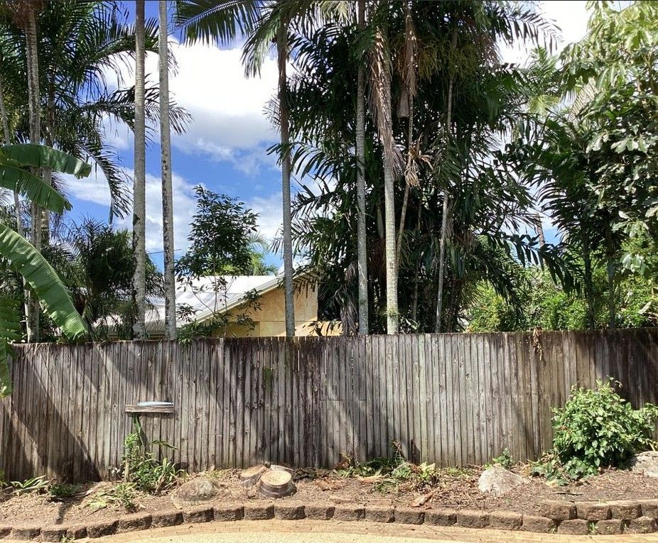 Pathway alongside a brown fence and green grass, trees, and a mountain under cloudy sky.