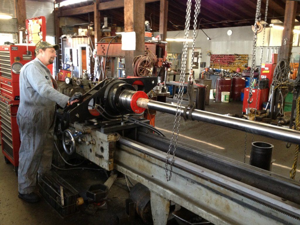 Hydraulic Equipment Repair — Man Operating Hydraulic Machine in Kelso, WA Man working on a lathe in a machine shop. Gray jumpsuit, turning a metal rod.