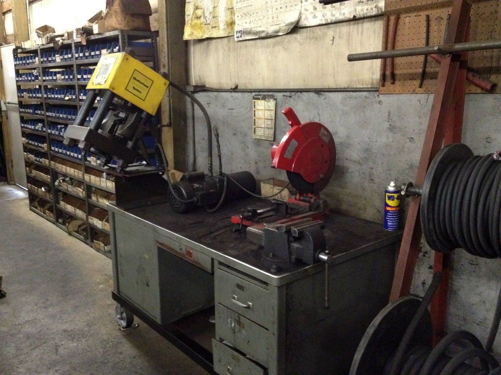 Metalworking workbench with a saw, vise, and welding equipment in a workshop.
