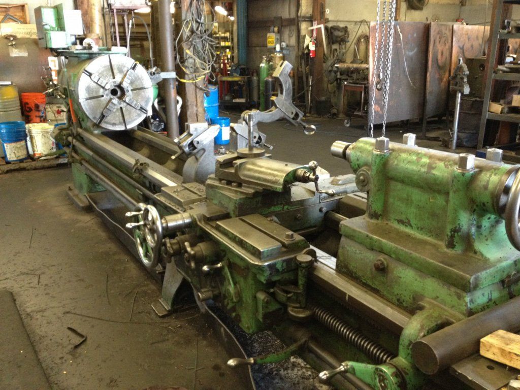 Hydraulic Equipment Manufacturers — Giant Hydraulic Machine in Kelso,WA A large green metal lathe machine in a workshop, with various tools and equipment in the background.