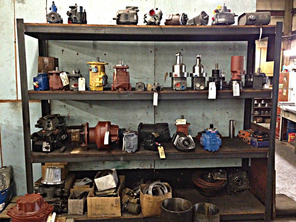 Metal shelf holding various machine parts in a workshop; parts are different colors.