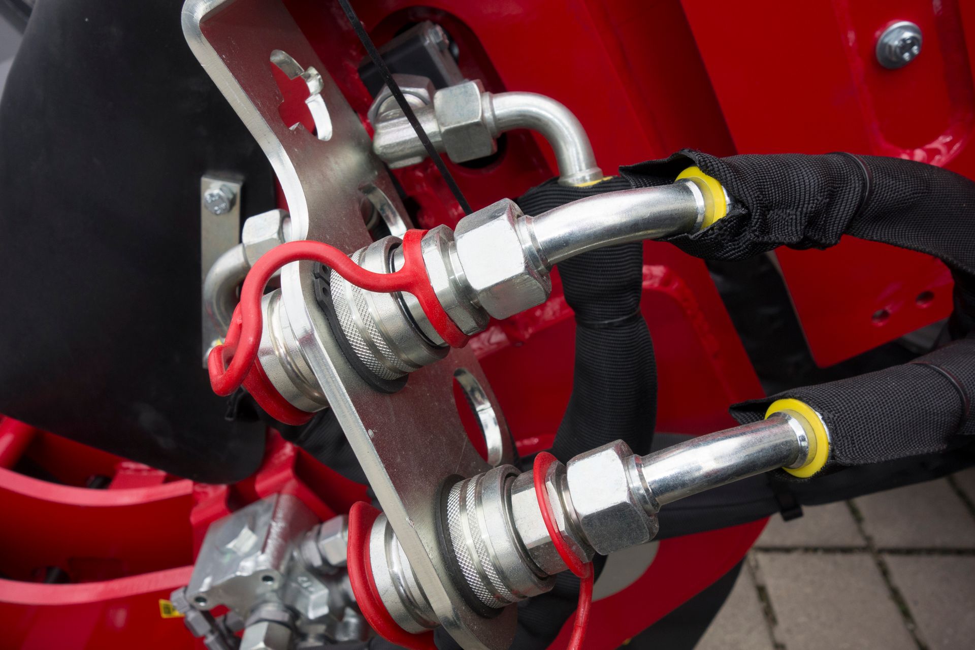 Close-up of hydraulic hoses and metal fittings connected to industrial machinery.
