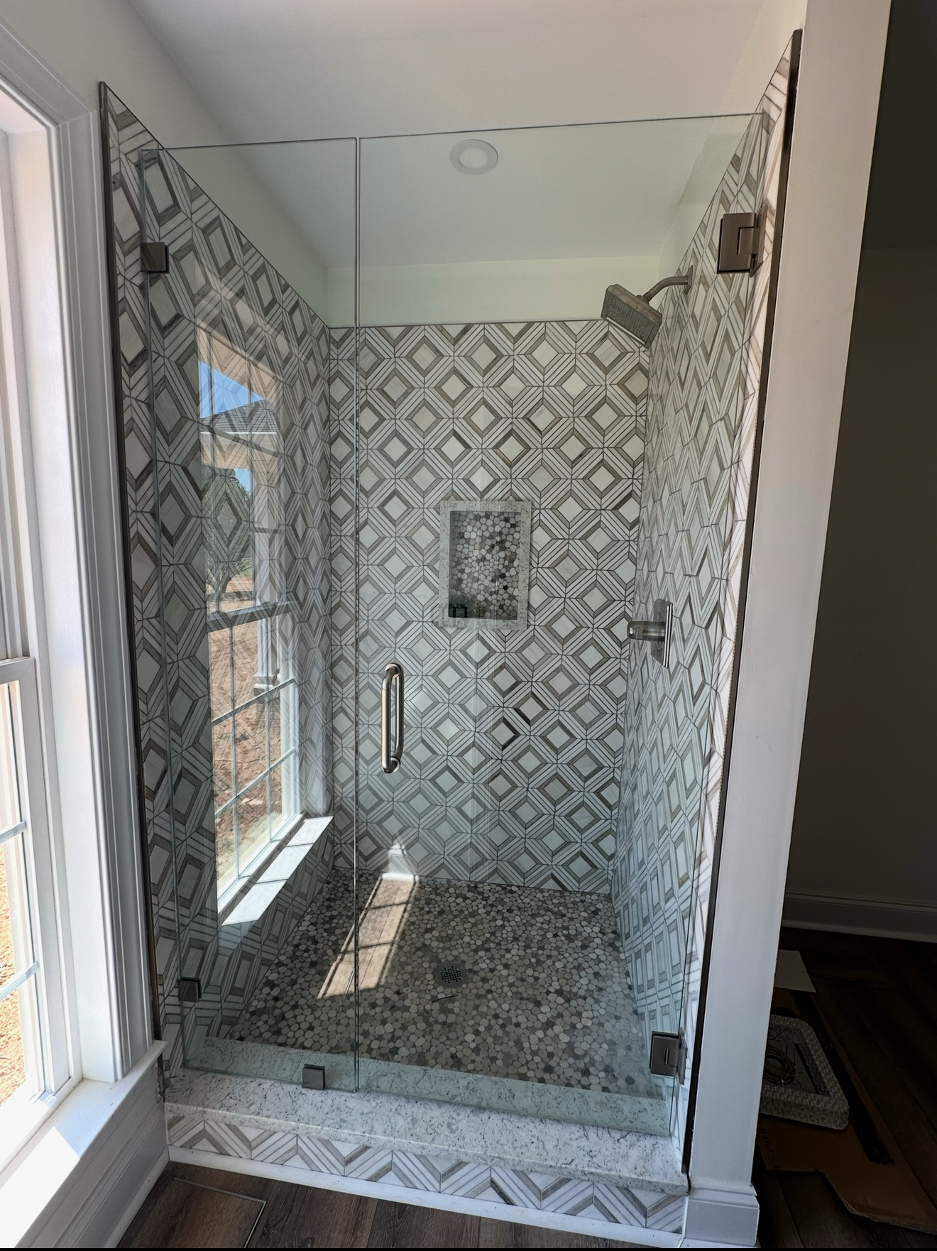 A shower stall with a glass door and a window in a bathroom.