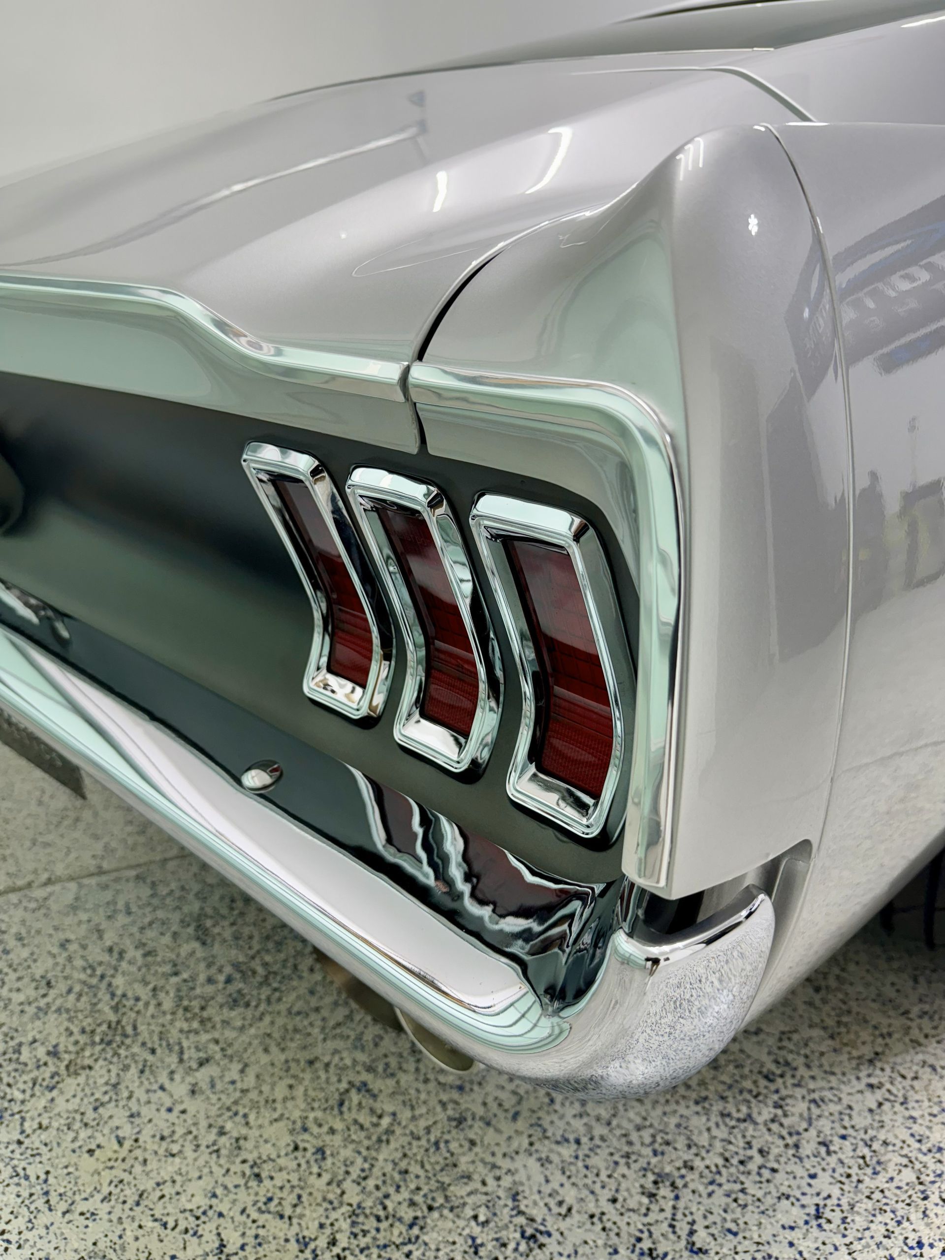 Chrome-trimmed rear of a silver vintage car, featuring three red taillights against a black panel.