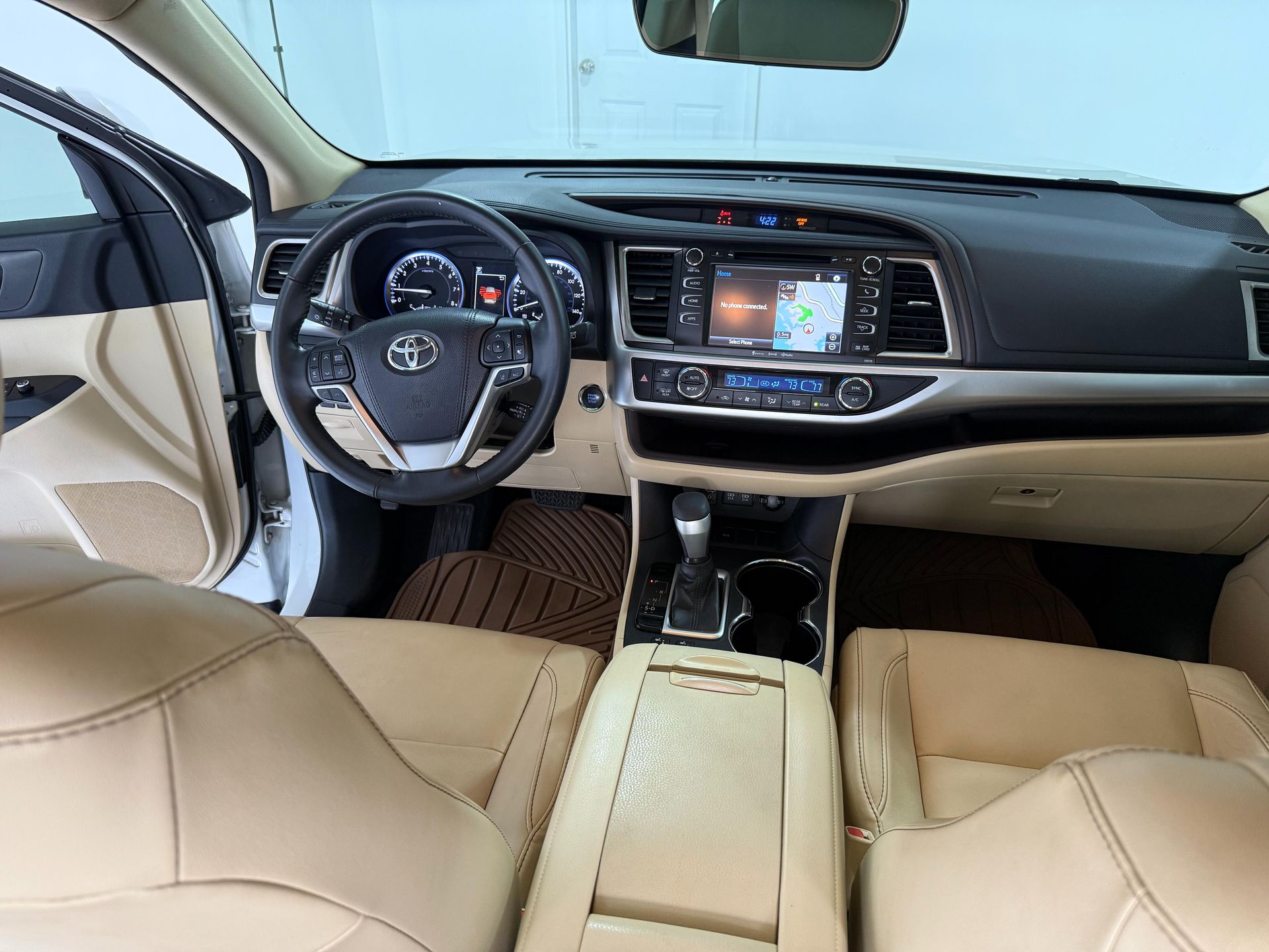 Interior view of a beige Toyota Highlander's dashboard, steering wheel, and front seats.
