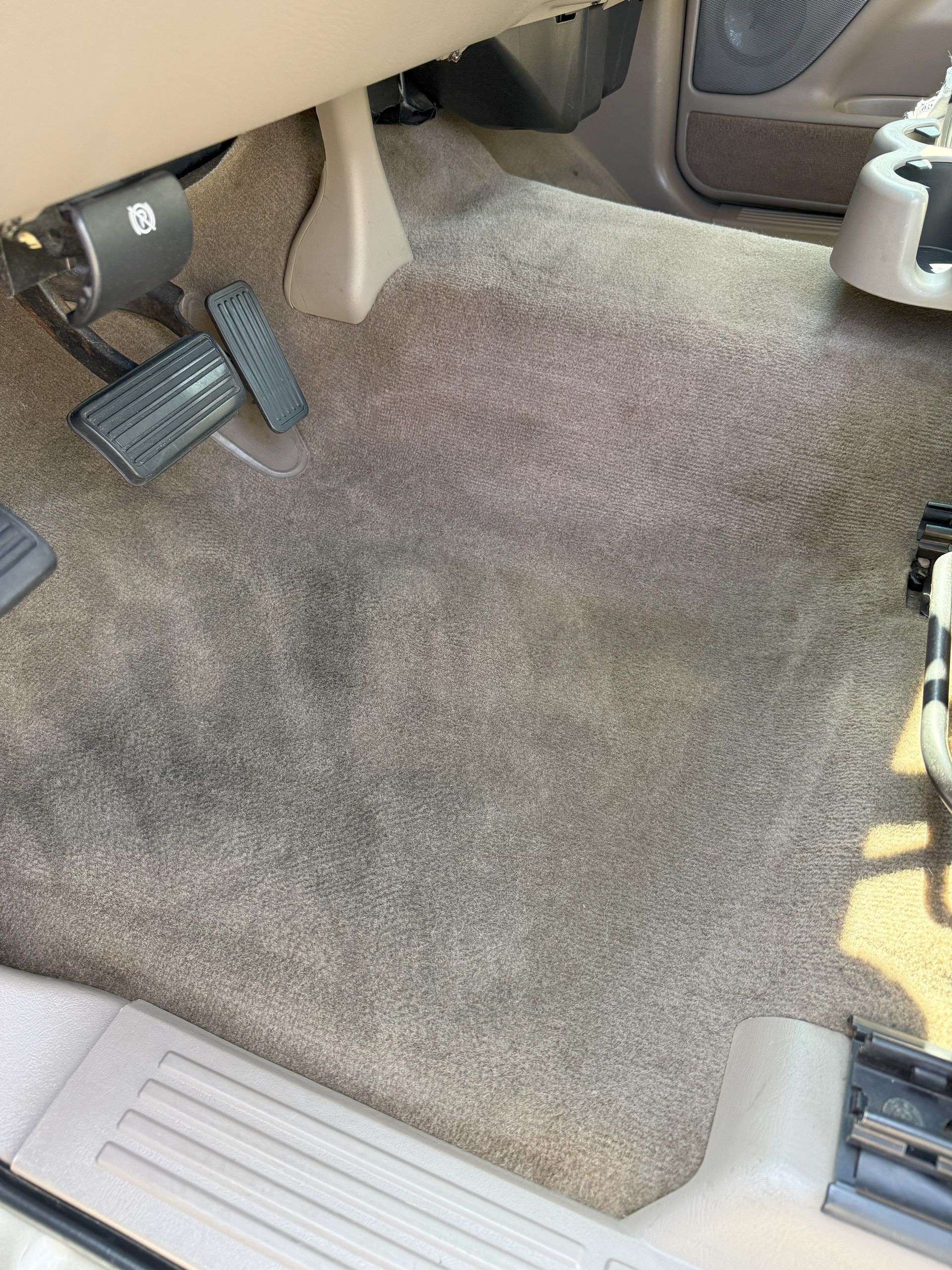 Tan car carpet, showing wear and stains around the pedals.