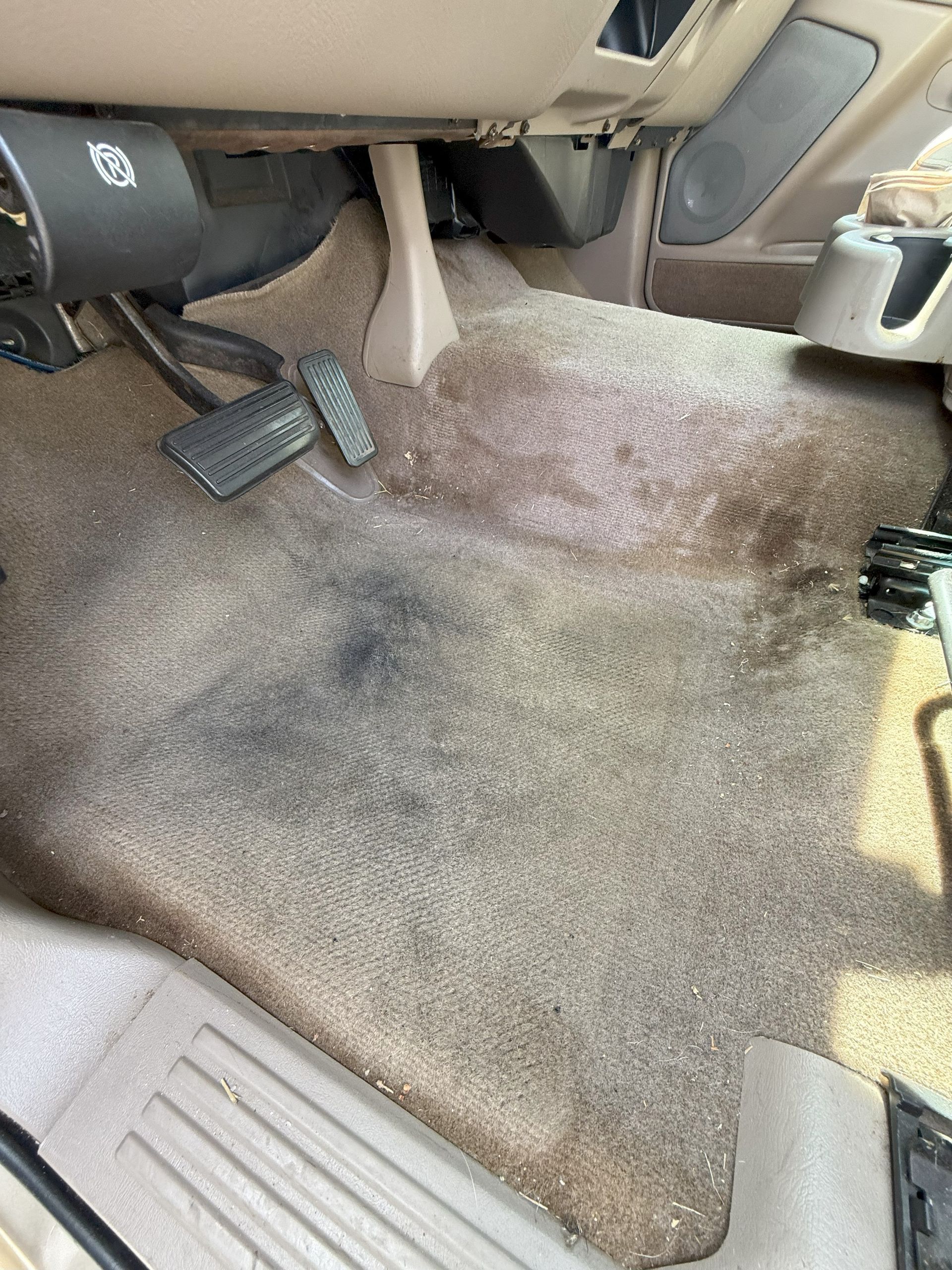 Beige car interior with stained carpet near pedals.